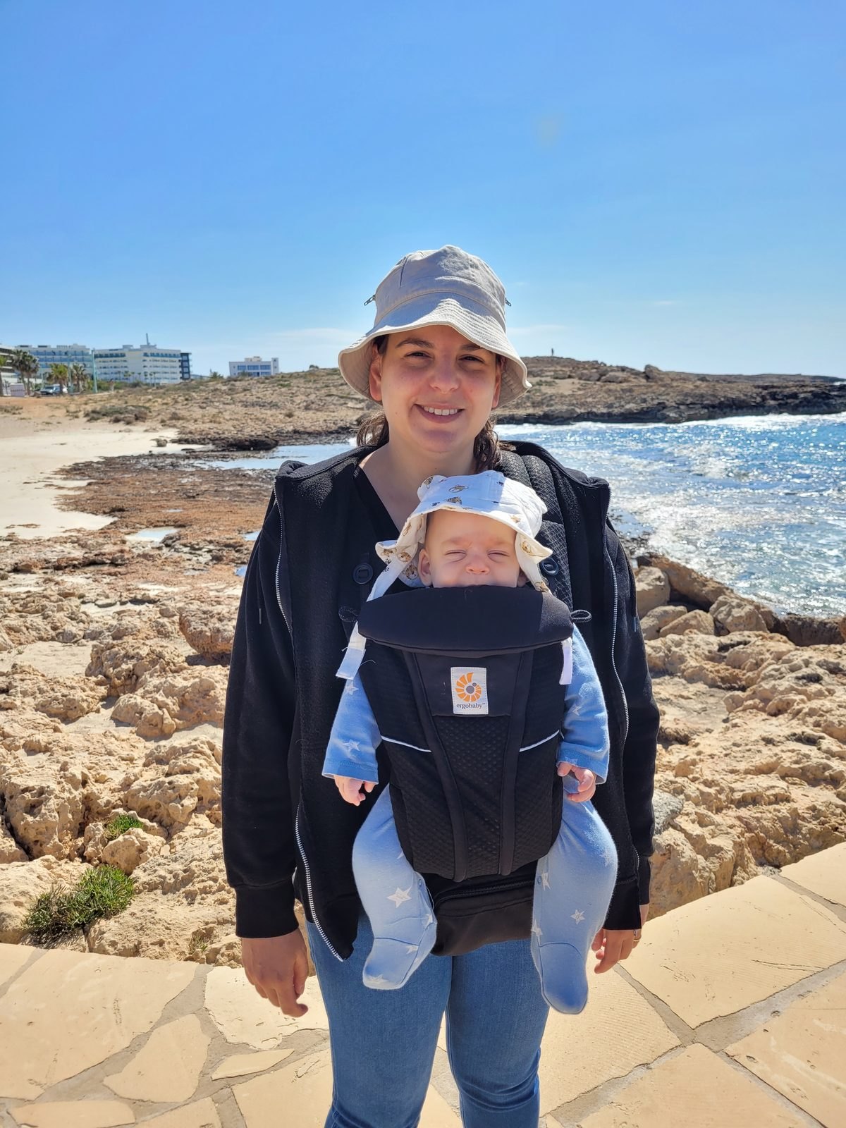 אמא עם תינוק במנשא על חוף סלעי